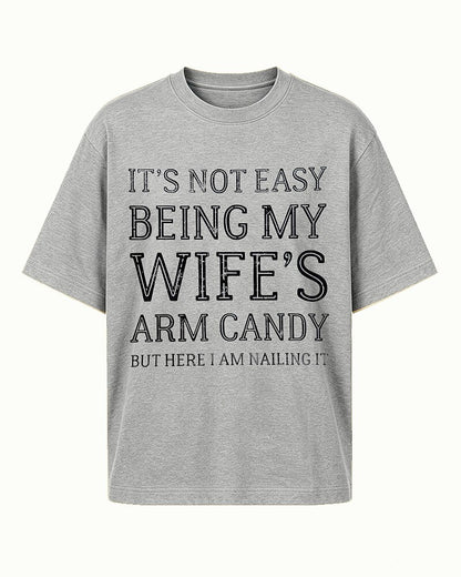 It's Not Easy Being My Wife's Arm Candy, but Here I Am Nailing It quote on Apricot cotton T-shirt